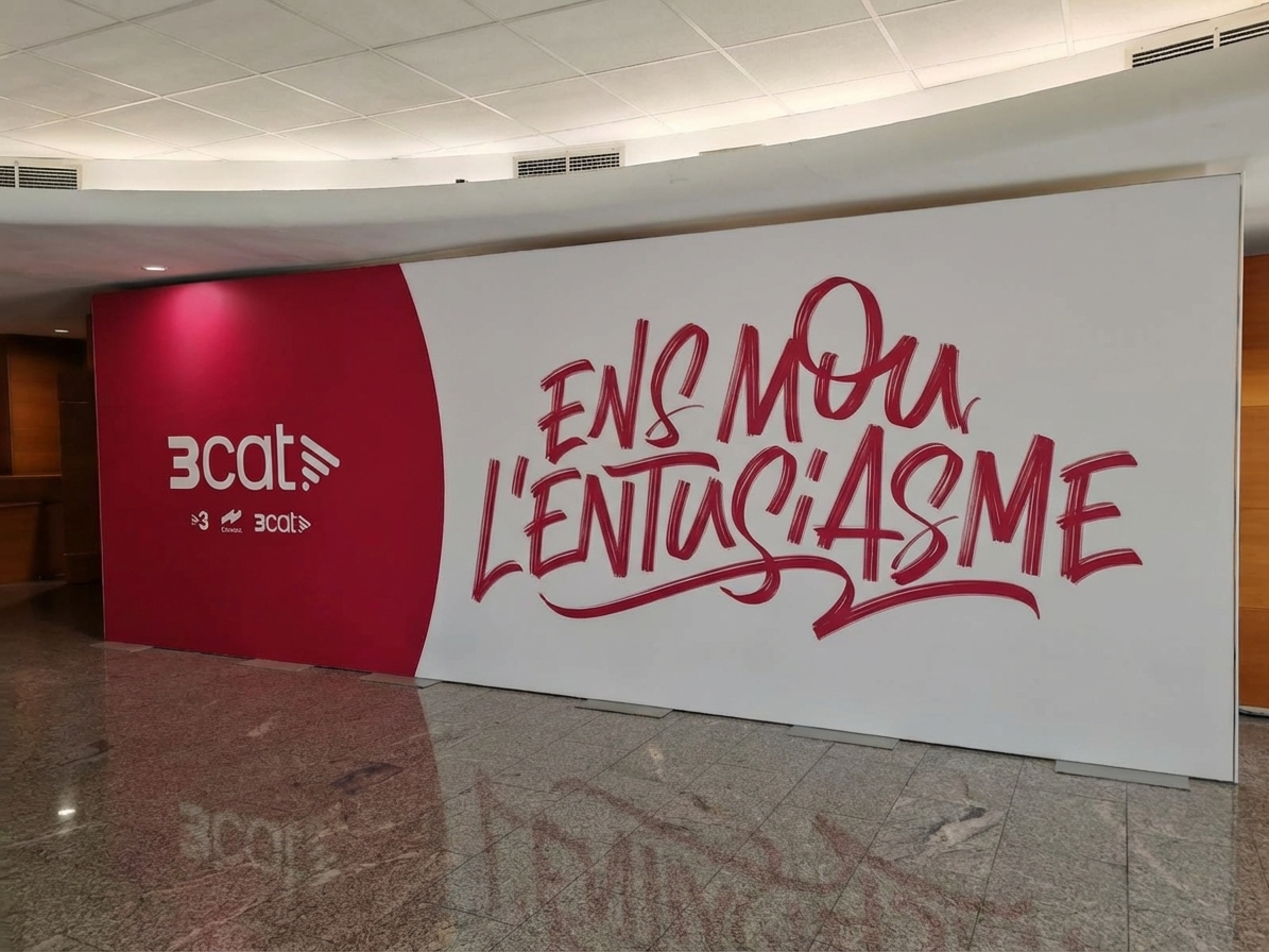 Mural corporativo 3cat con claim Ens Mou L'Entusiasme en vinilo rojo y blanco instalado en hall interior