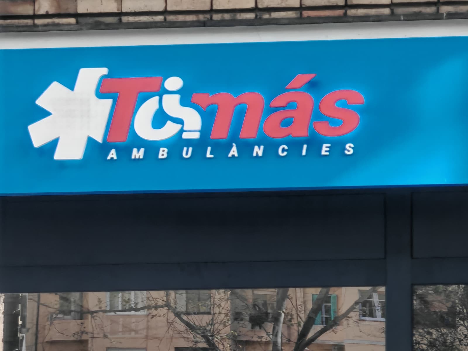 Rótulo retroiluminado Ambulàncies Tomàs con caja de luz LED azul y letras corpóreas 3D rojo y blanco en fachada