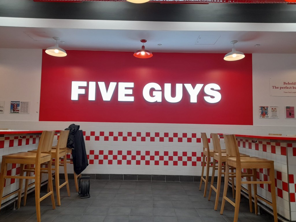 Vista frontal del rótulo luminoso Five Guys en área de comedor