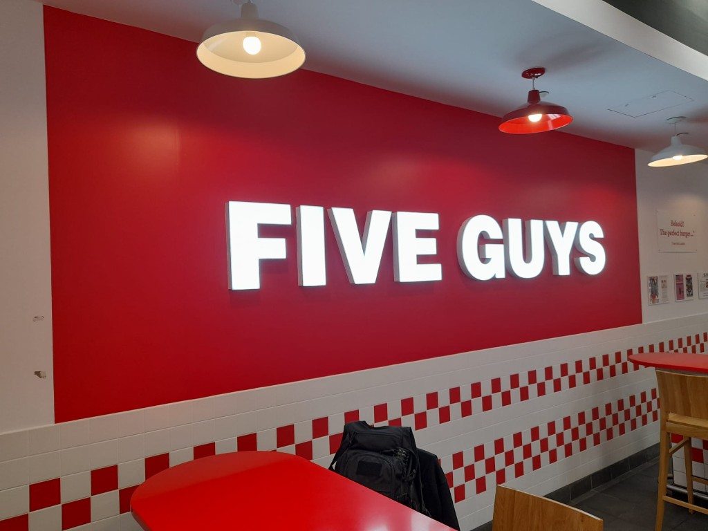 Rótulo luminoso Five Guys integrado en pared roja interior del restaurante