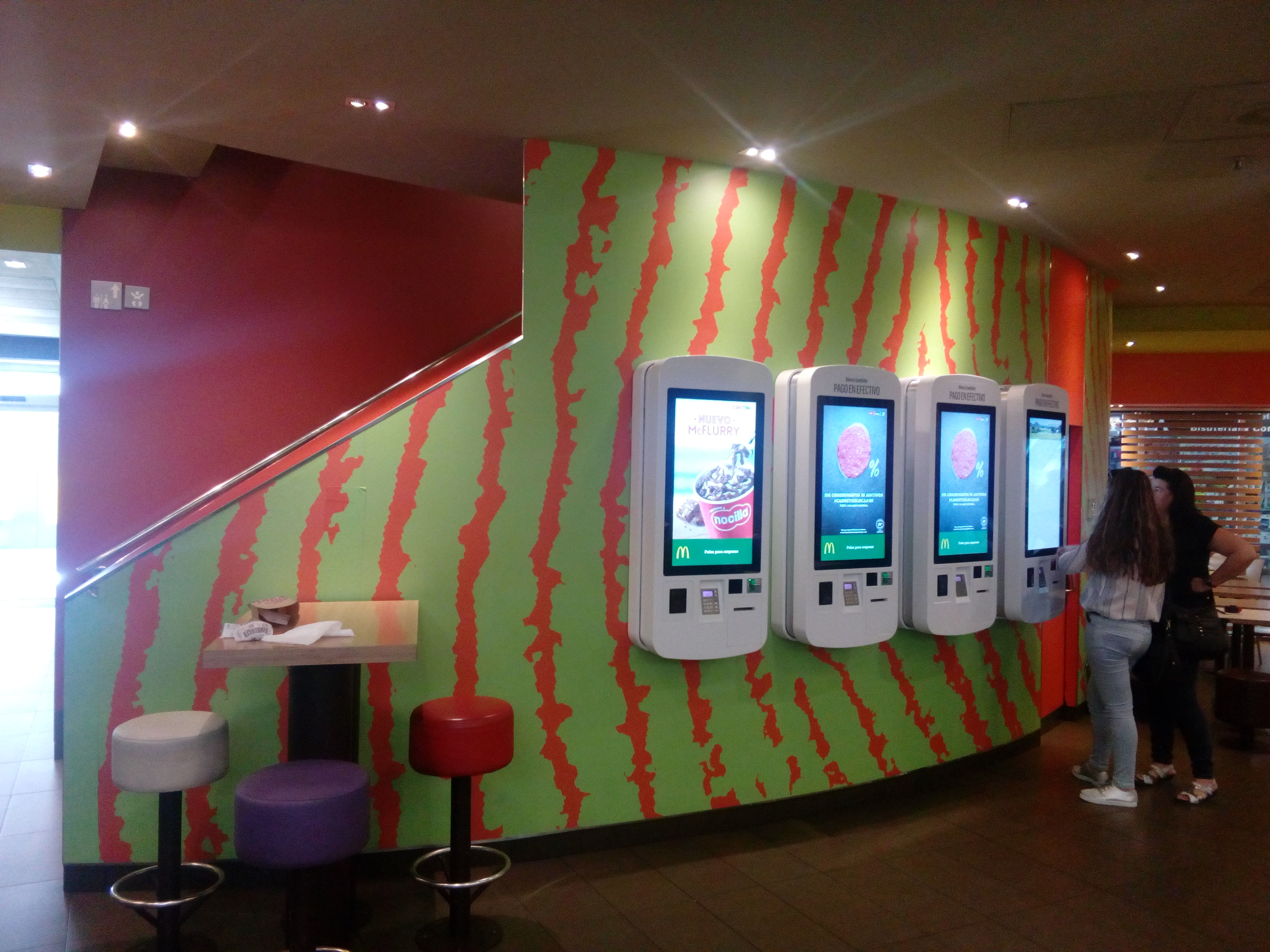 Pared decorativa con patrón de sandías y kioscos de autoservicio en restaurante McDonald's