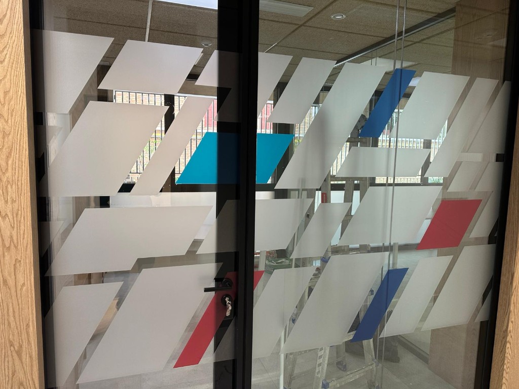 Detalle de mampara de cristal vinilada con formas geométricas y colores corporativos
