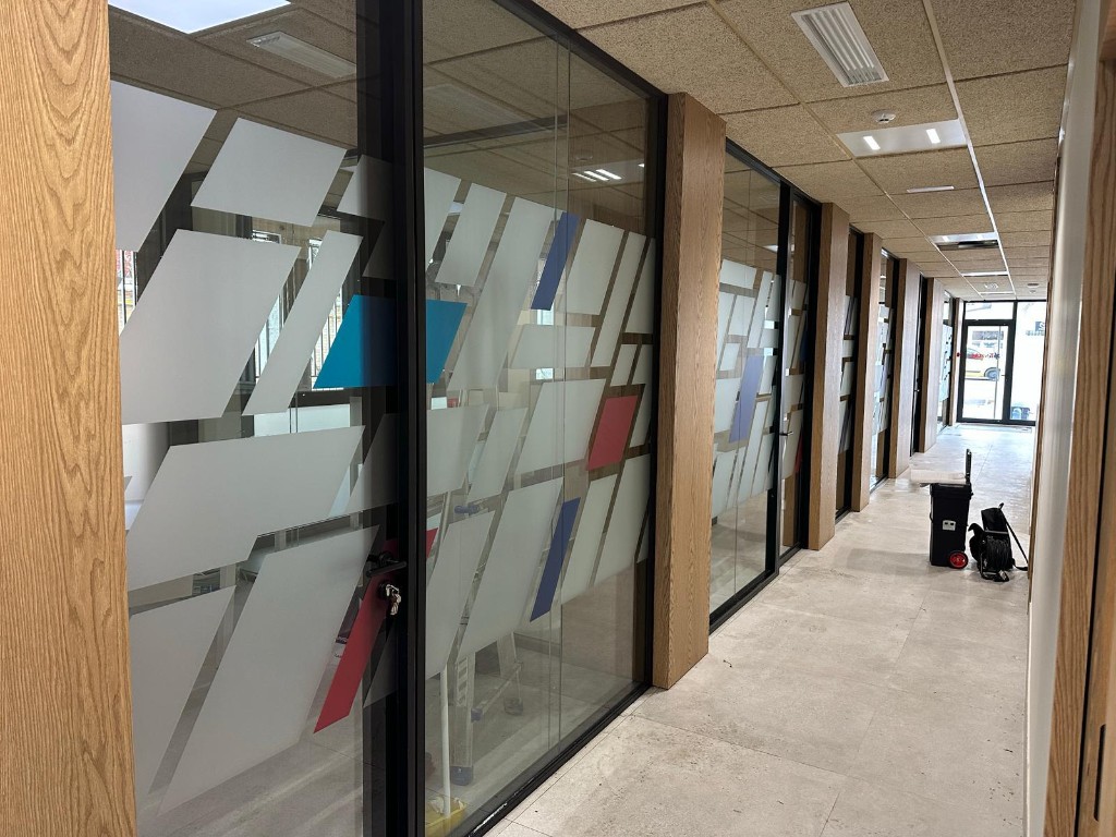 Vista lateral de pasillo de oficinas con mamparas de vidrio viniladas