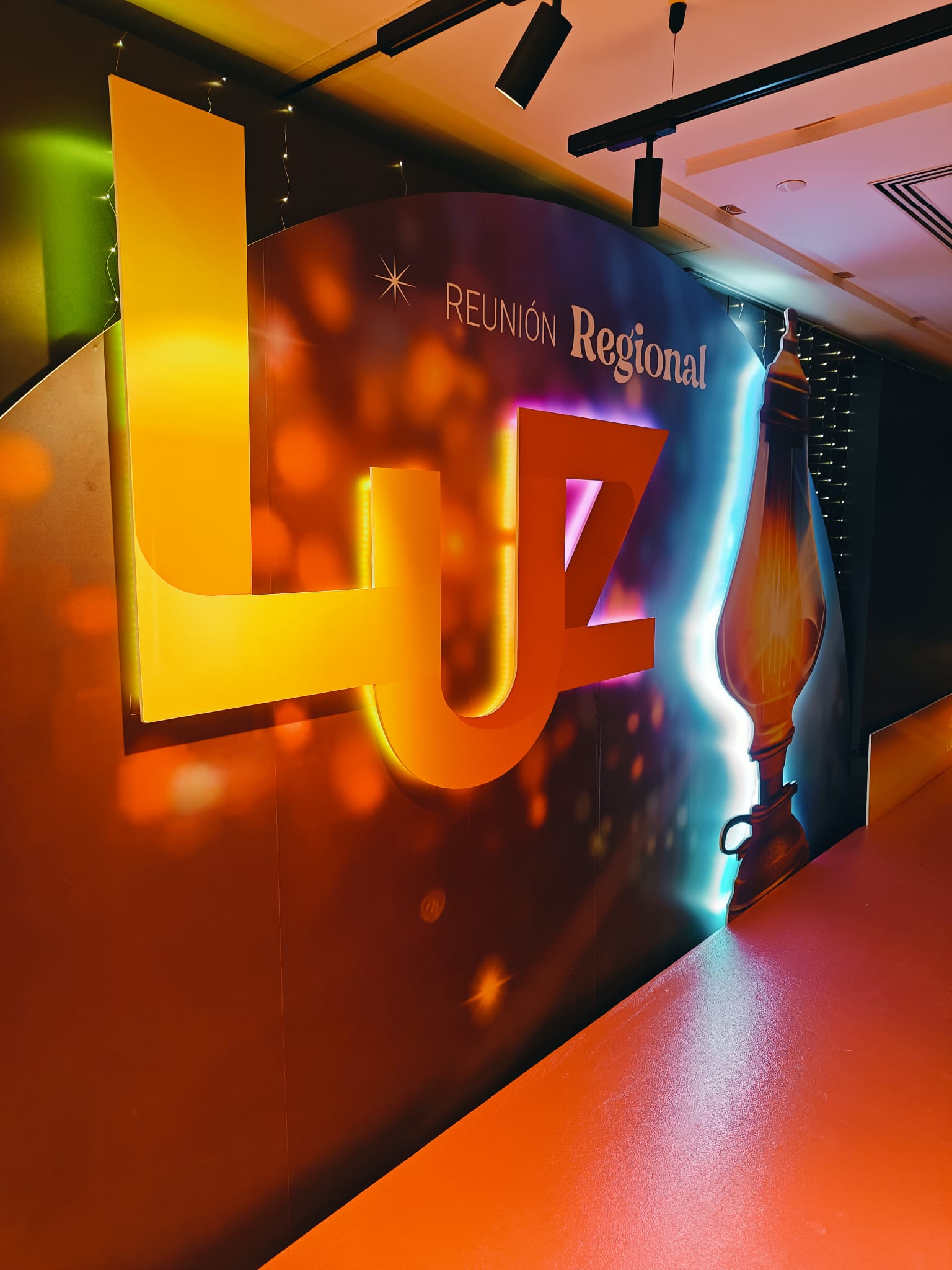 Escenografía Reunión Regional LUZ con letras corpóreas 3D doradas retroiluminadas y backdrop de gran formato con lámpara y luces bokeh