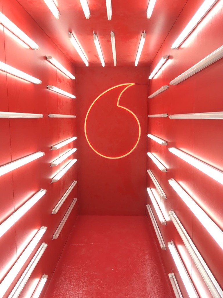 Túnel temático de Vodafone con iluminación lineal y logotipo en neón